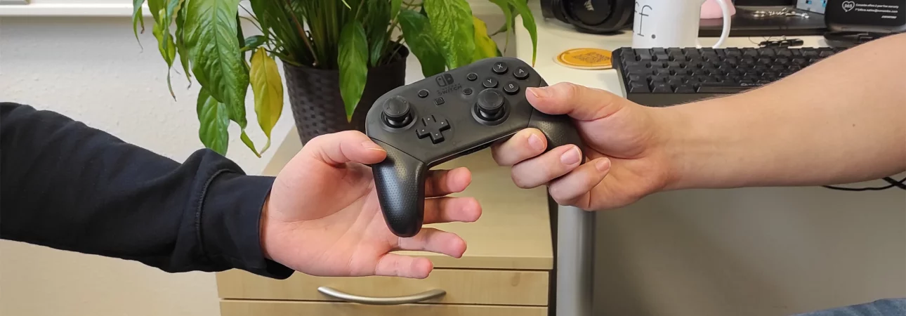 Eine Hand, die einer anderen einen Switch Controller reicht